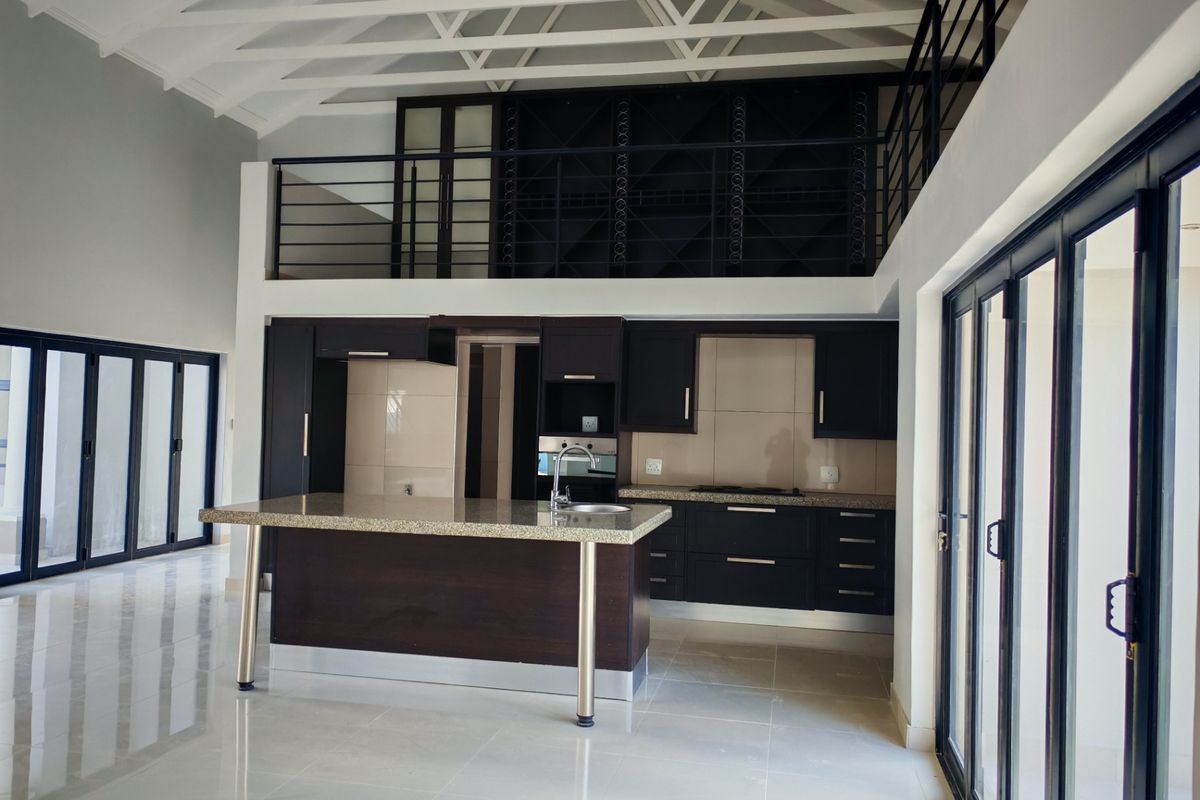 Modern open-plan kitchen featuring dark cabinetry, granite countertops, a central island, and a mezzanine level with exposed rafters and large sliding glass doors.