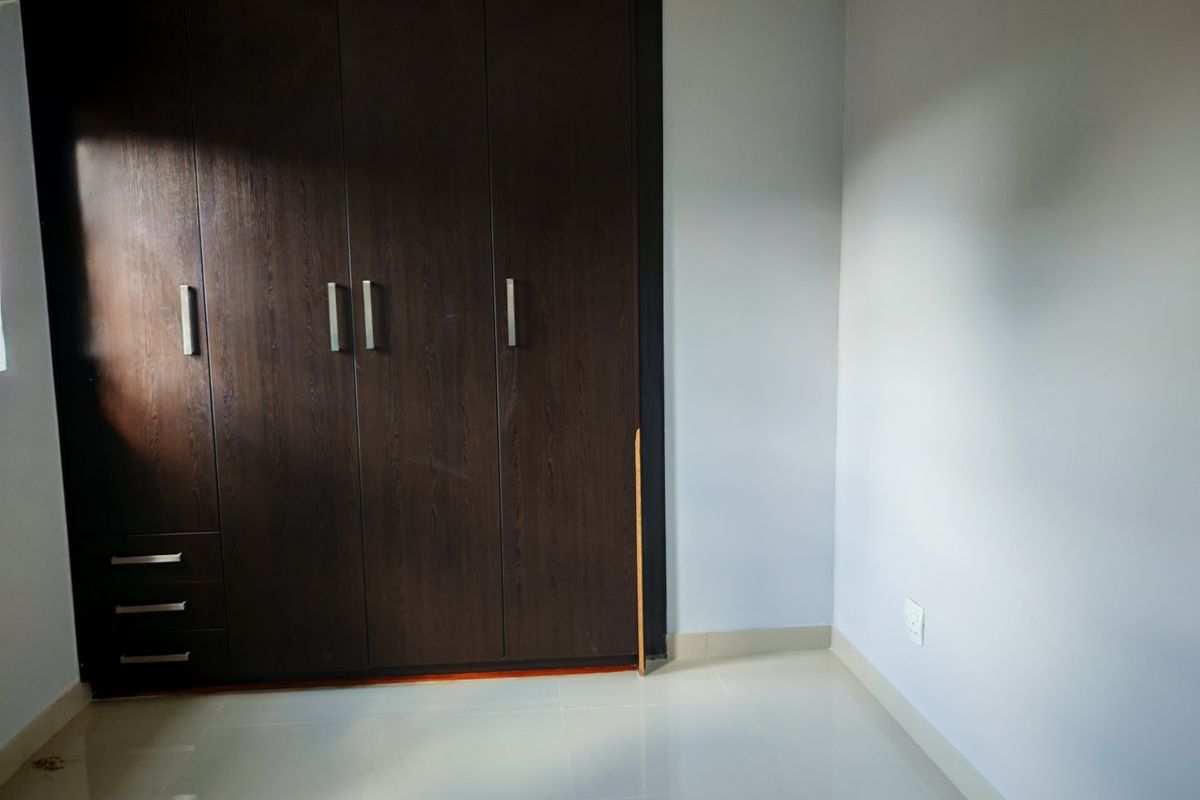 A bedroom featuring dark wood built-in wardrobes and neutral tiled flooring, offering a clean and functional space ready for personalization.