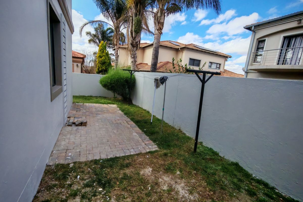 A compact rear garden area featuring a paved patio section, boundary wall, and a fixed washing line.