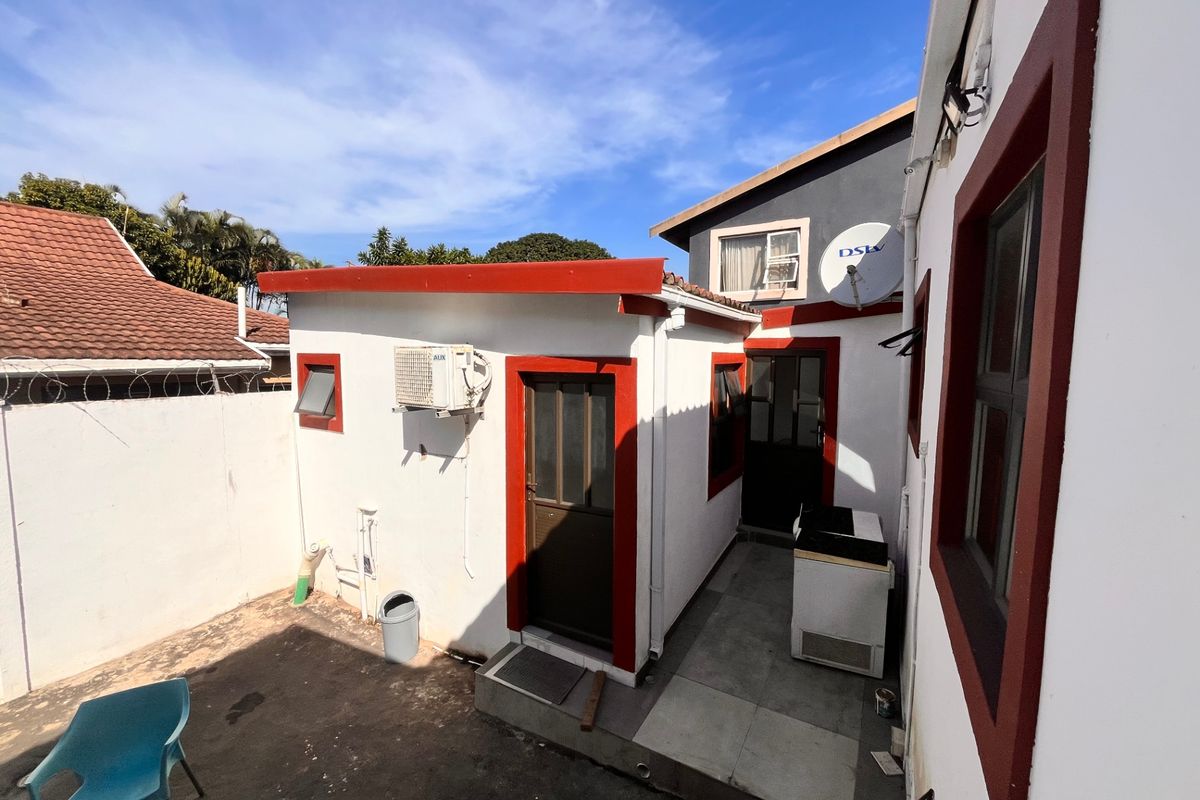 Rear courtyard area featuring paved flooring, exterior access doors, wall-mounted air conditioning unit, and perimeter security walling with razor wire.
