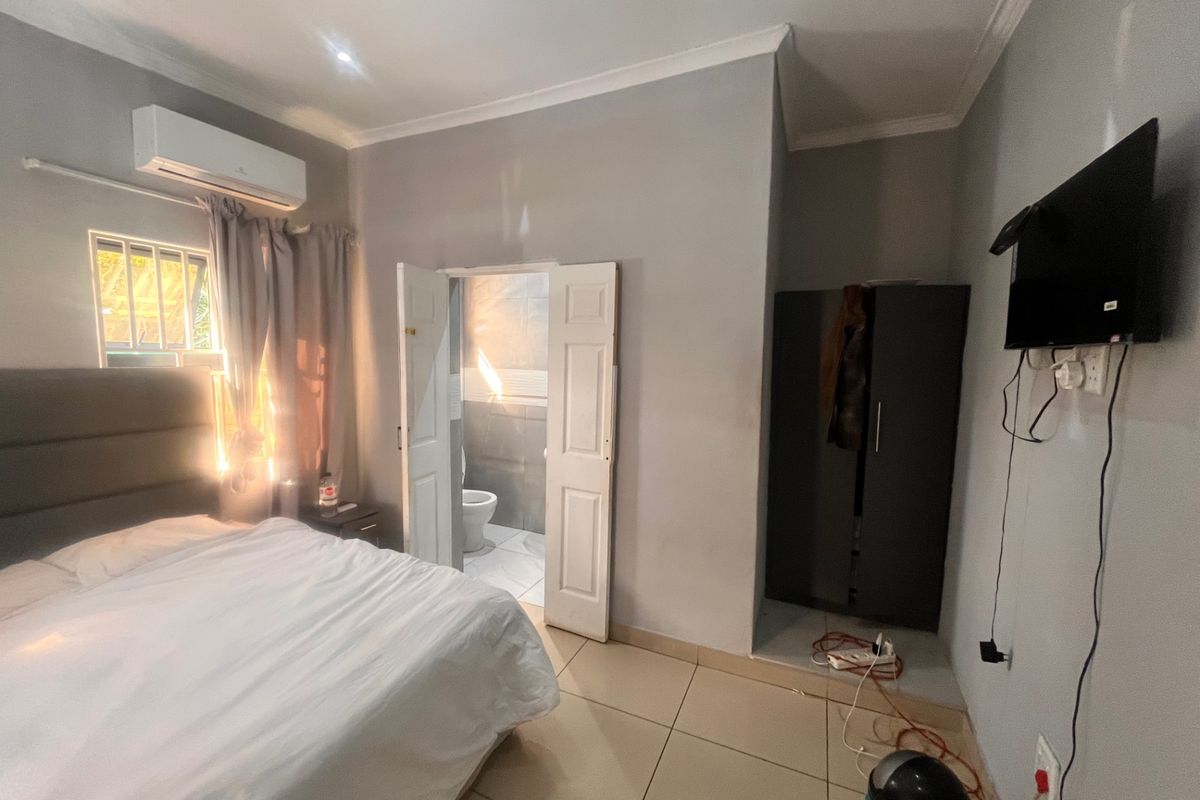 A bedroom featuring tiled flooring, an air conditioning unit, and an attached en-suite bathroom with a window security grill.