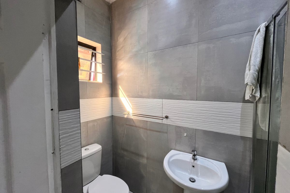 A modern bathroom featuring grey tiled walls, a pedestal basin, a toilet, and a glass-enclosed shower.
