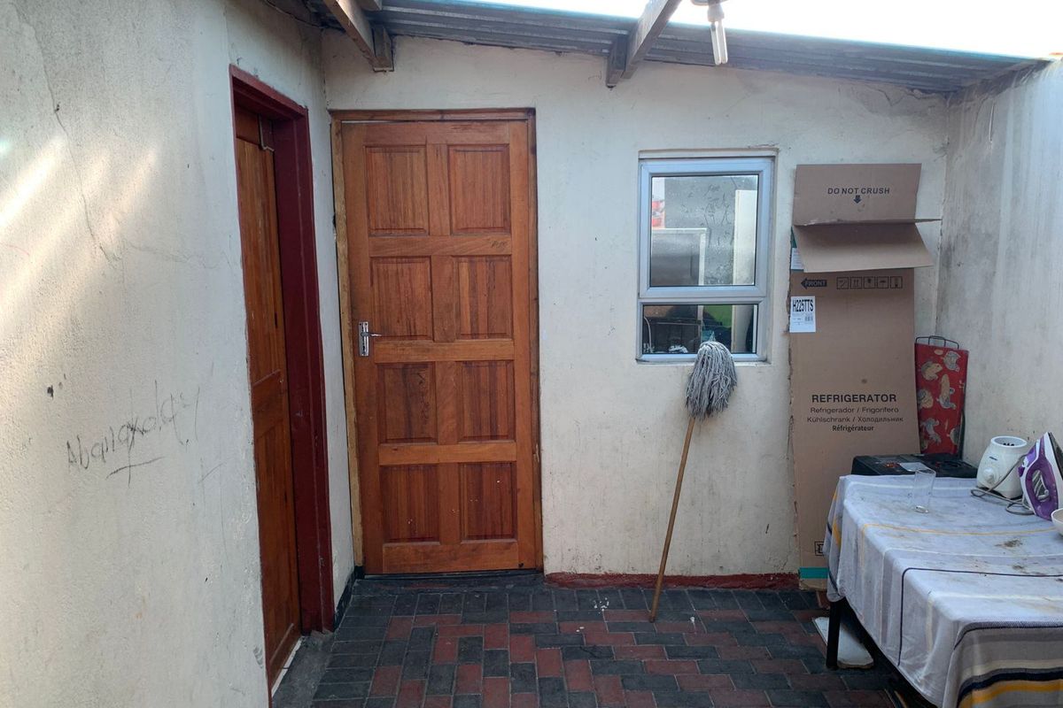 A covered outdoor patio area featuring paved flooring, timber doors, and a translucent roof, currently showing signs of wear and wall damage.