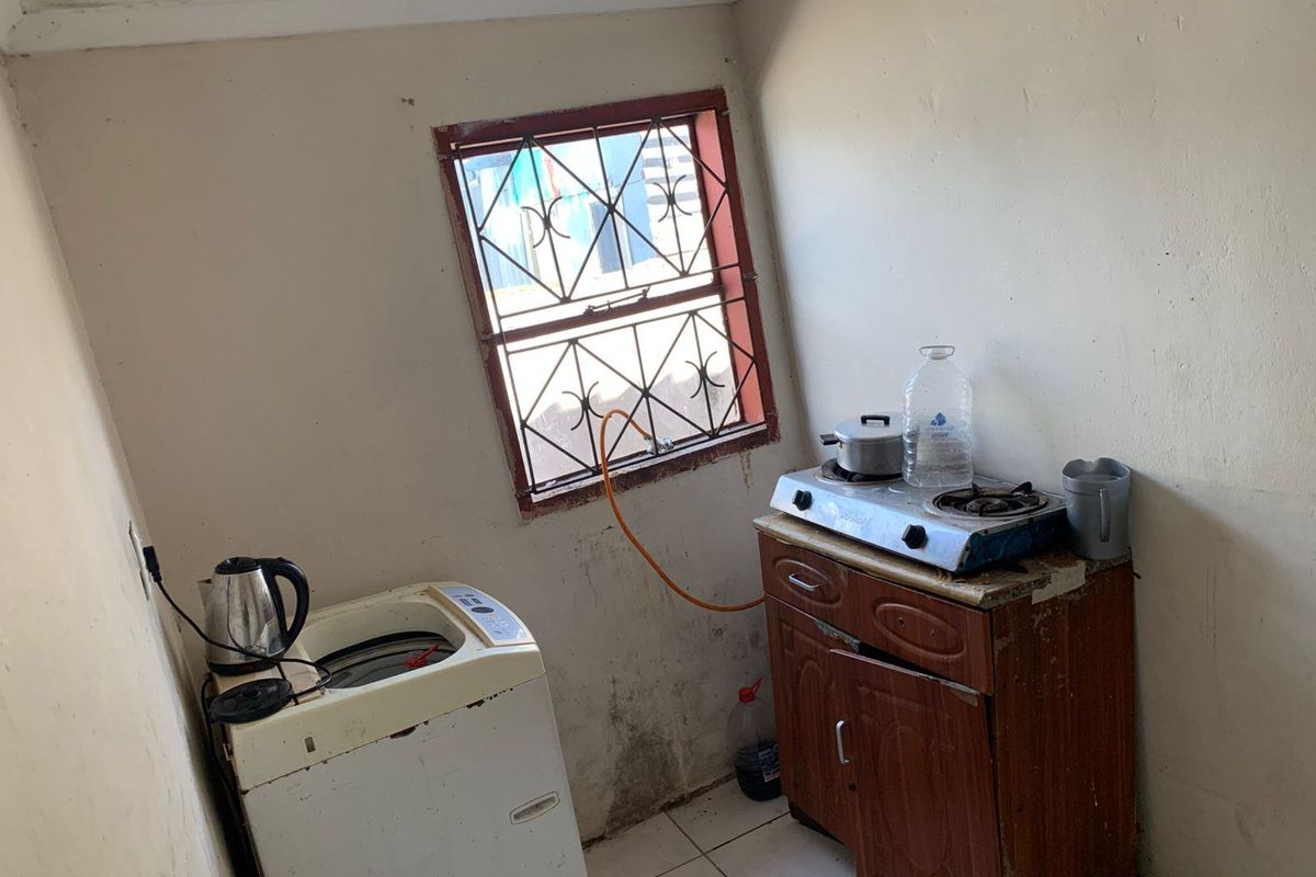 A compact kitchen area featuring tiled flooring, a window with security bars, and a basic gas hob setup.