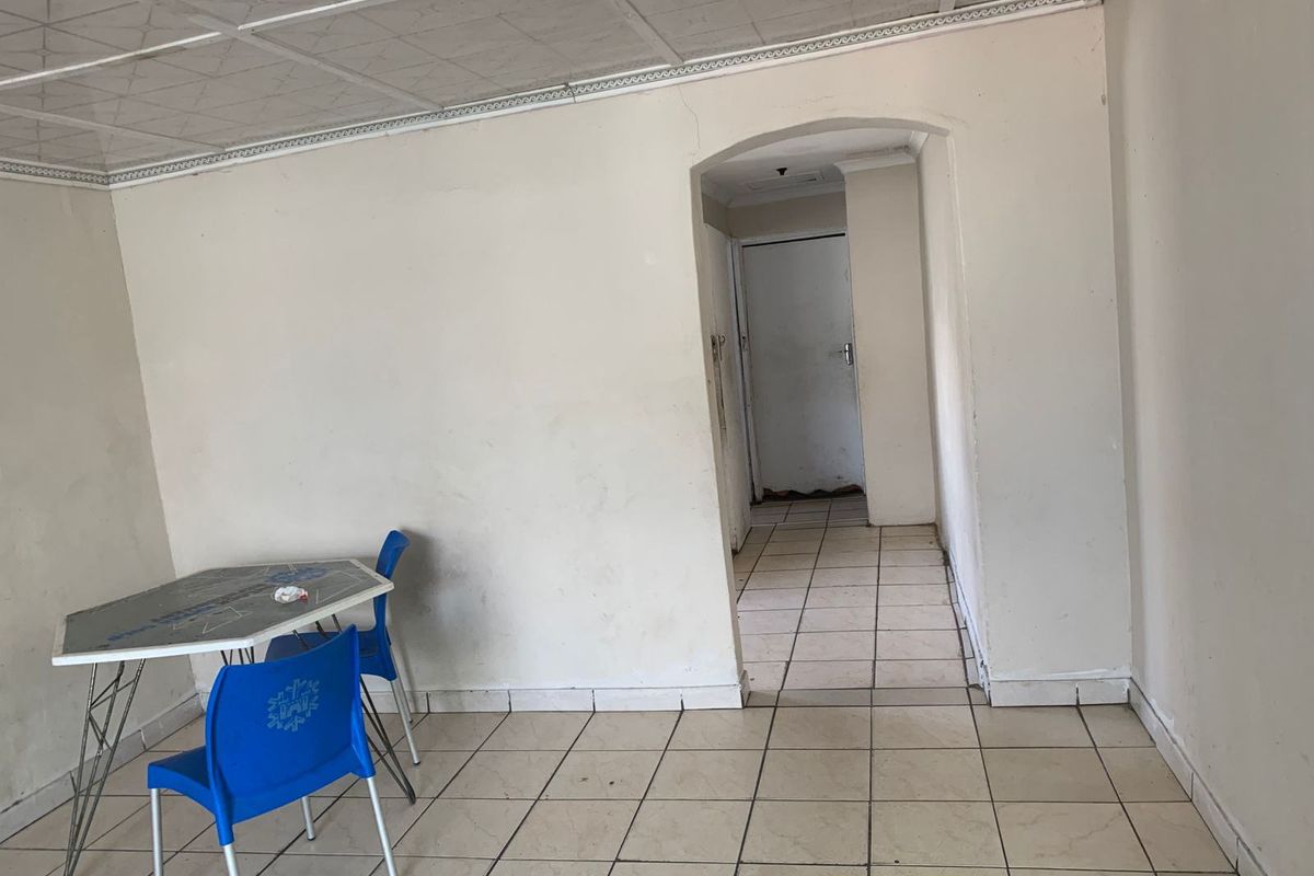 An empty living area featuring tiled flooring, an arched doorway, and a suspended ceiling, requiring cosmetic updates and wall repairs.