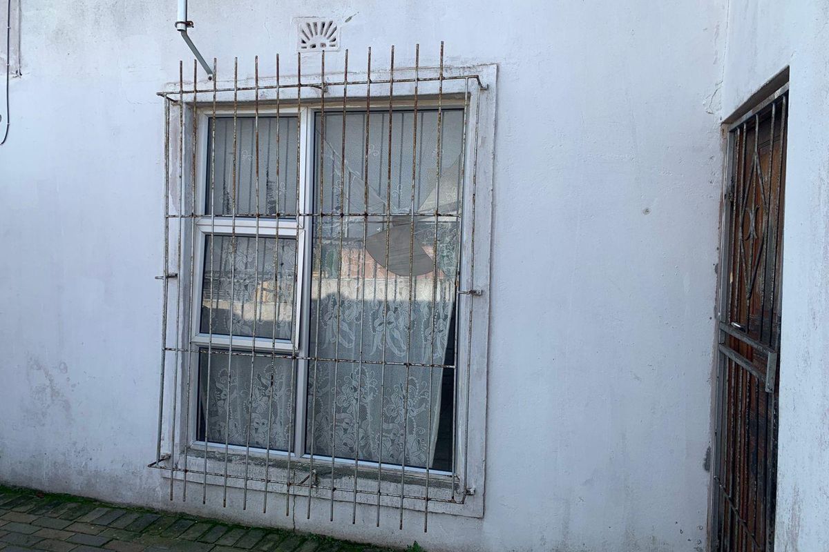 Exterior rear view showing a window with security bars, paved ground, and visible signs of wear on the building facade.