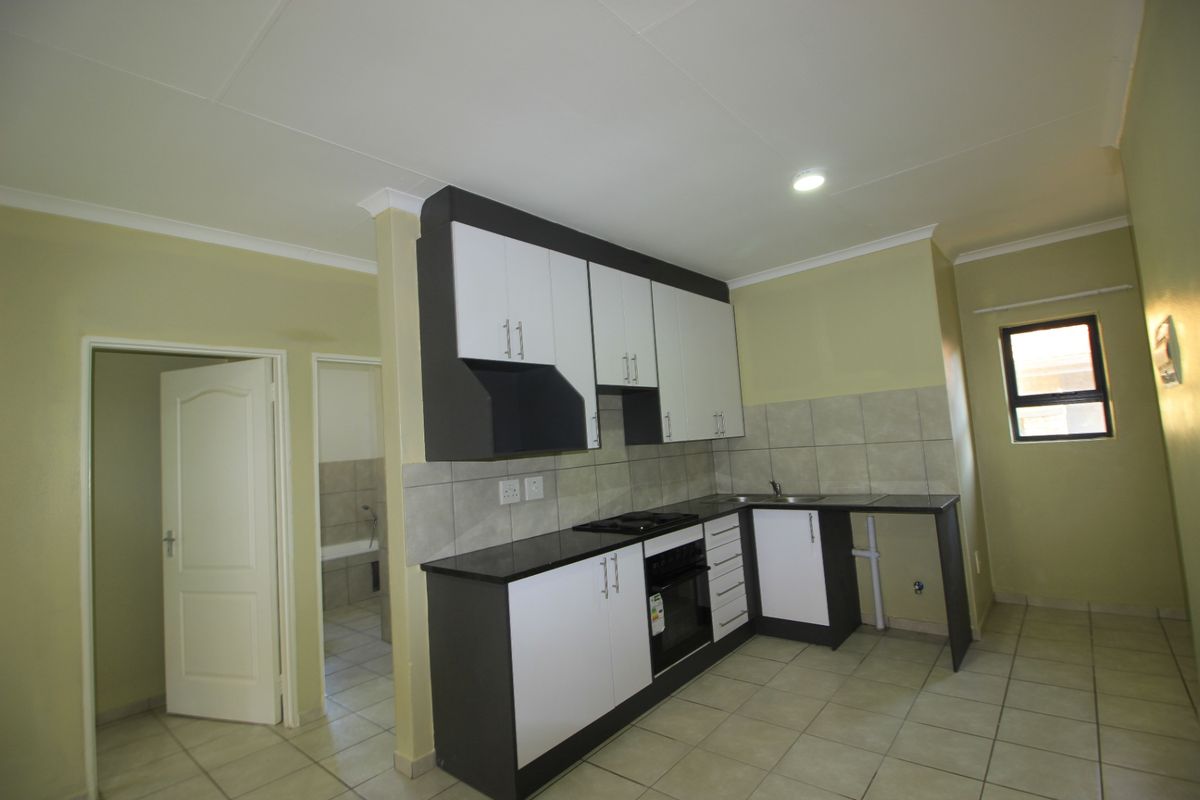 A functional kitchen featuring modern two-tone cabinetry, granite countertops, built-in oven and hob, and neutral tiled flooring.