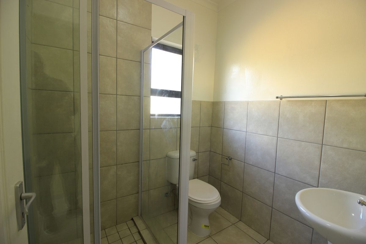 A functional bathroom featuring a glass-enclosed shower, a standard toilet, and a wall-mounted basin with neutral tiled finishes throughout.