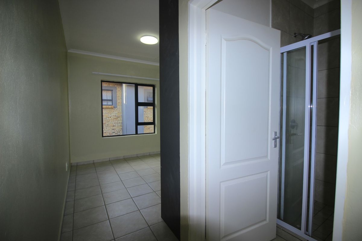 An empty bedroom featuring tiled flooring, a window with an aluminium frame, and an adjacent en-suite shower area.