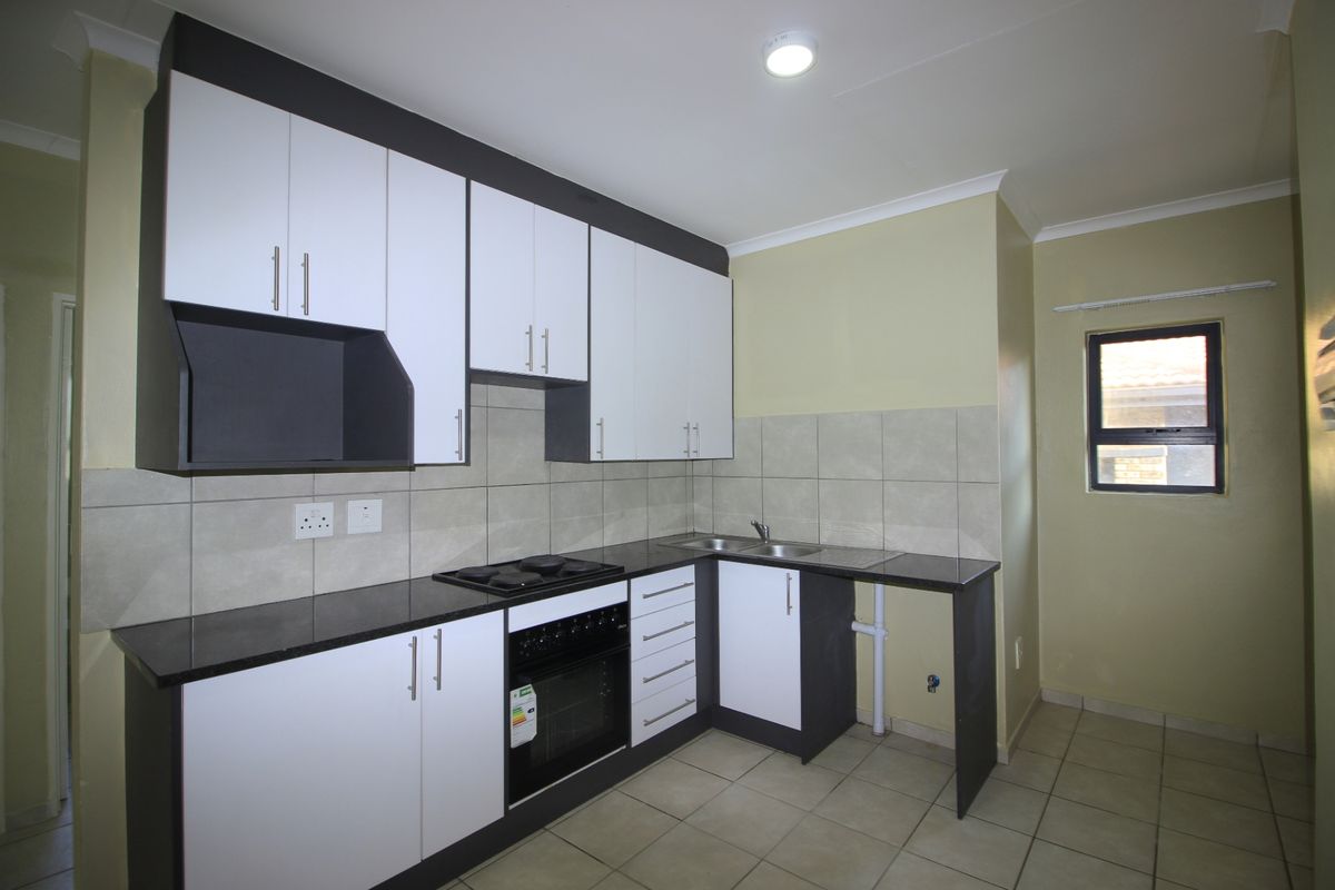 A clean, modern kitchen featuring white and dark cabinetry, black granite countertops, built-in oven, electric hob, and tiled finishes throughout.
