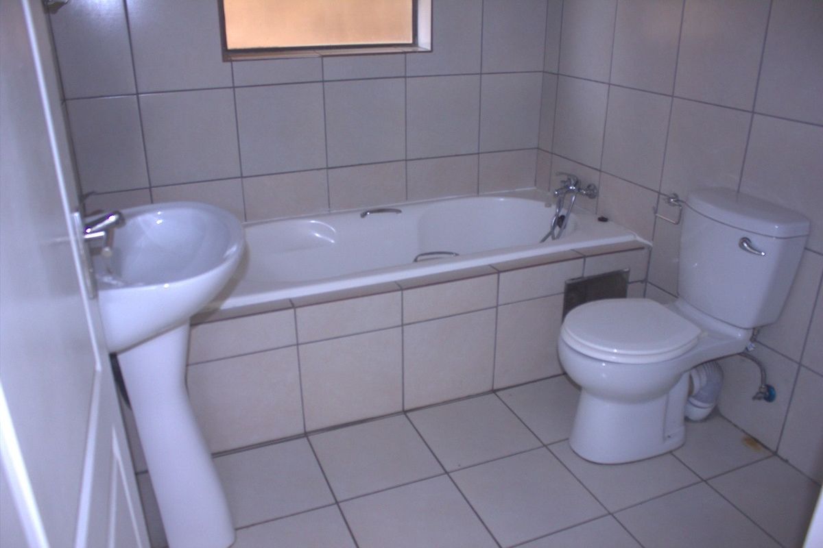 A functional bathroom featuring a pedestal basin, built-in bathtub, and toilet with neutral ceramic tiling throughout.
