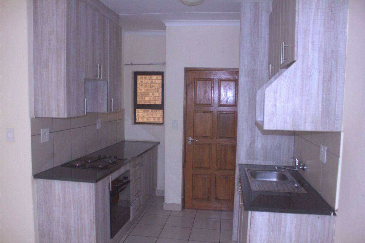A functional kitchen featuring light wood-look cabinetry, dark countertops, a built-in oven with gas hob, and tiled flooring.