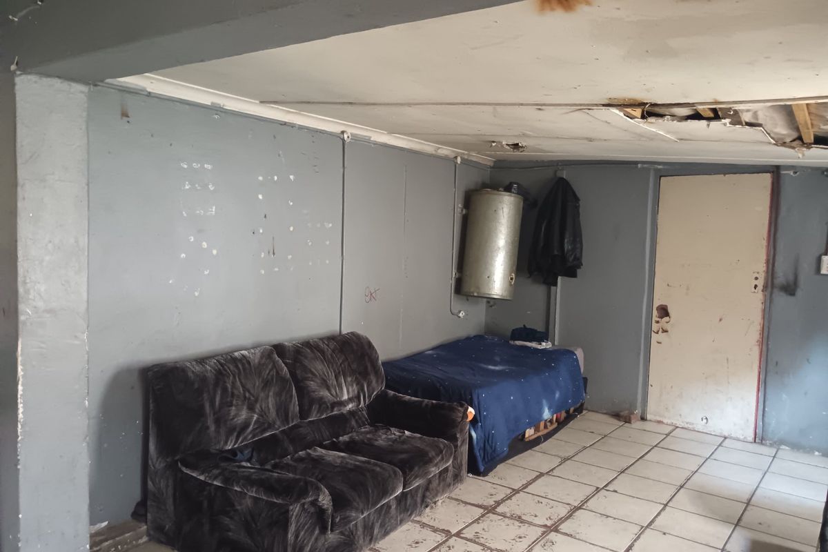 A living area in poor condition featuring tiled flooring, an exposed ceiling with water damage, and visible wall wear, requiring significant renovation.