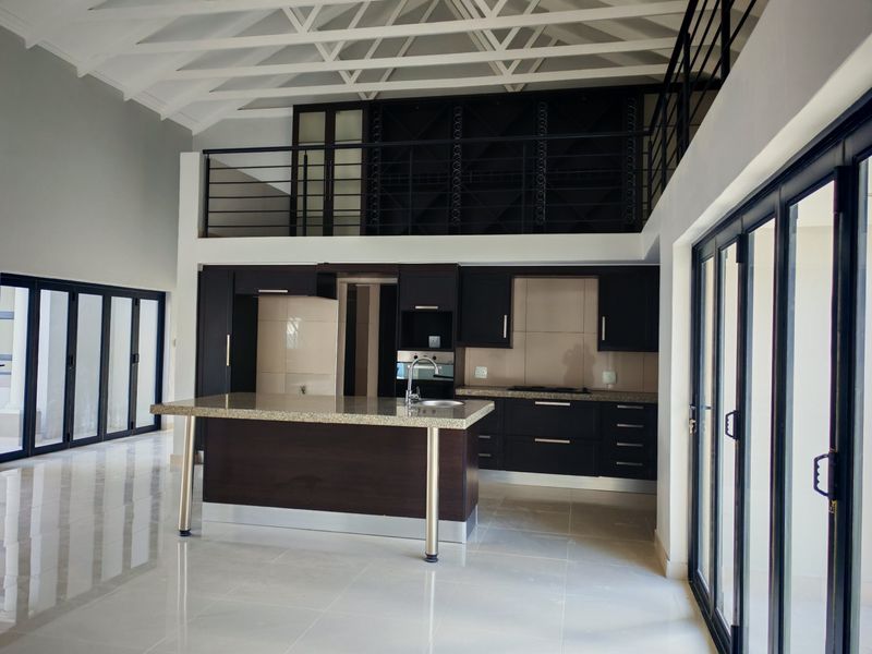 Spacious open-plan kitchen featuring dark cabinetry, granite countertops, and a central island, set under a vaulted ceiling with an overlooking mezzanine level.
