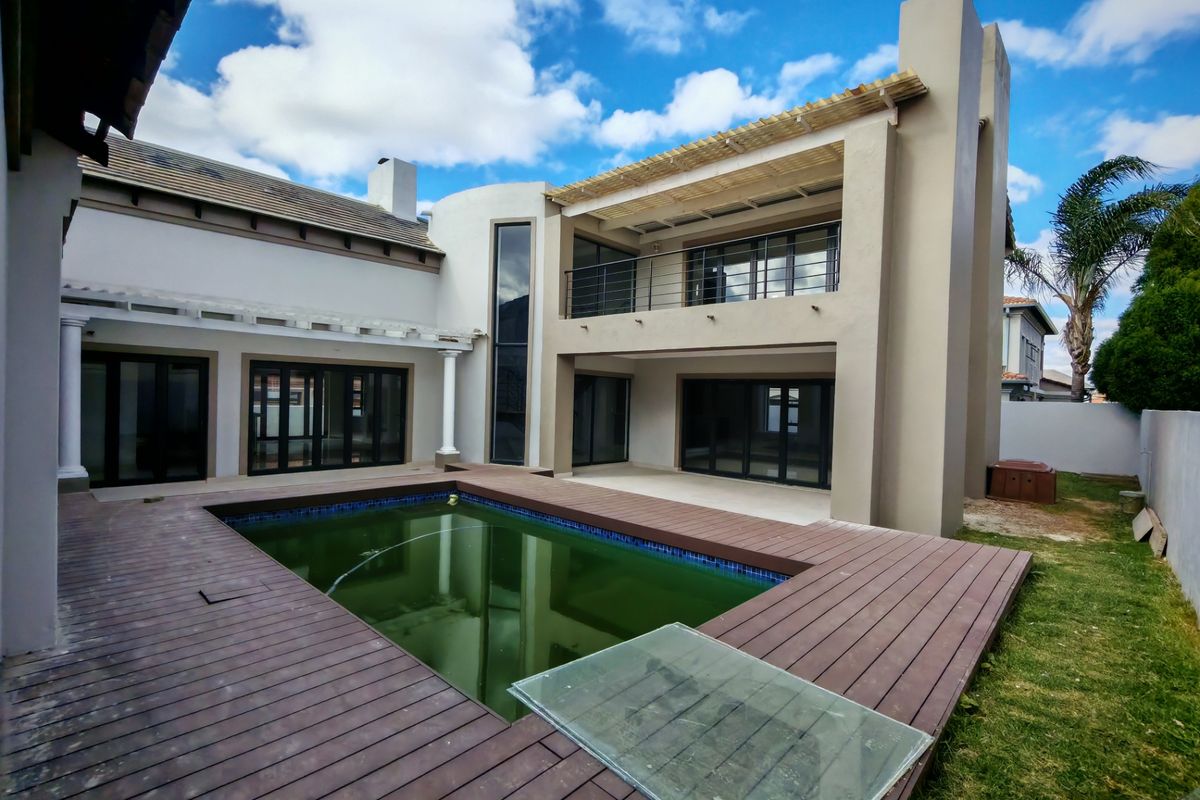 Rear exterior view featuring a swimming pool with timber decking, a covered patio, and a balcony on the upper level.