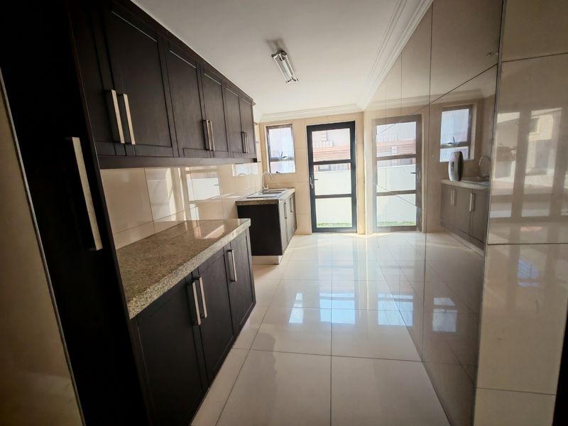 A clean, modern scullery featuring dark wood cabinetry, granite countertops, a stainless steel sink, and polished floor tiles with direct outdoor access.