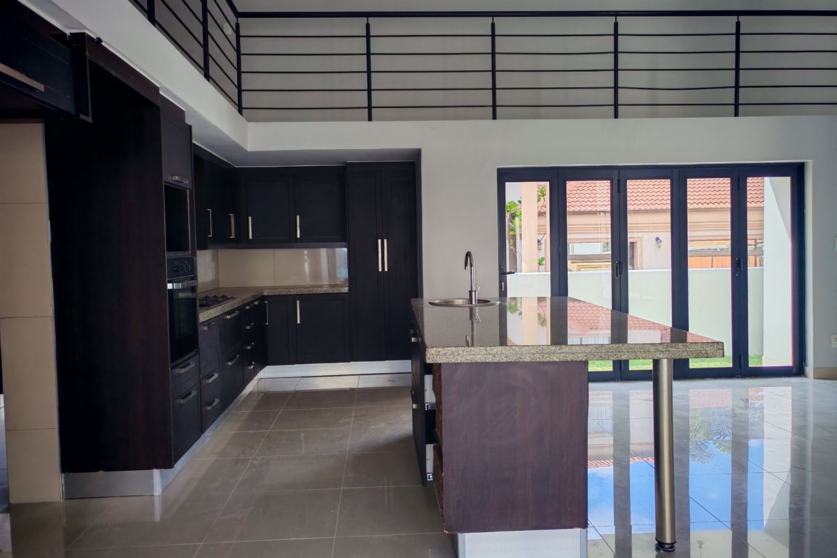 Modern open-plan kitchen featuring dark cabinetry, granite countertops, a central island, and folding glass doors leading to the exterior, with a mezzanine level above.