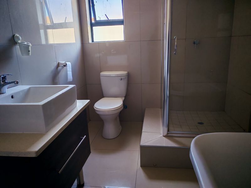 A clean, modern bathroom featuring a vanity with a vessel sink, a toilet, and a separate glass-enclosed shower with neutral wall and floor tiling.