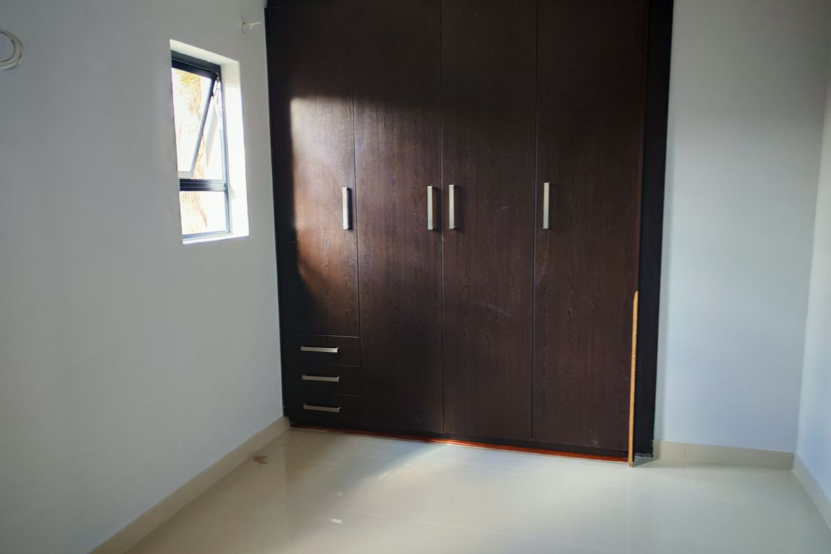 A clean, empty bedroom featuring dark wood built-in cupboards, tiled flooring, and a small casement window.