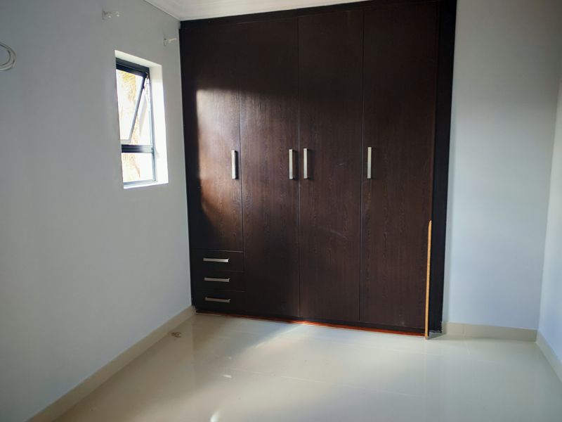 A clean, empty bedroom featuring dark wood built-in cupboards, tiled flooring, and a small casement window.