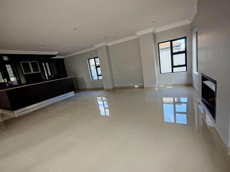 Spacious open-plan living area featuring polished tiled floors, a built-in fireplace, and a modern kitchen with dark cabinetry and a central island.