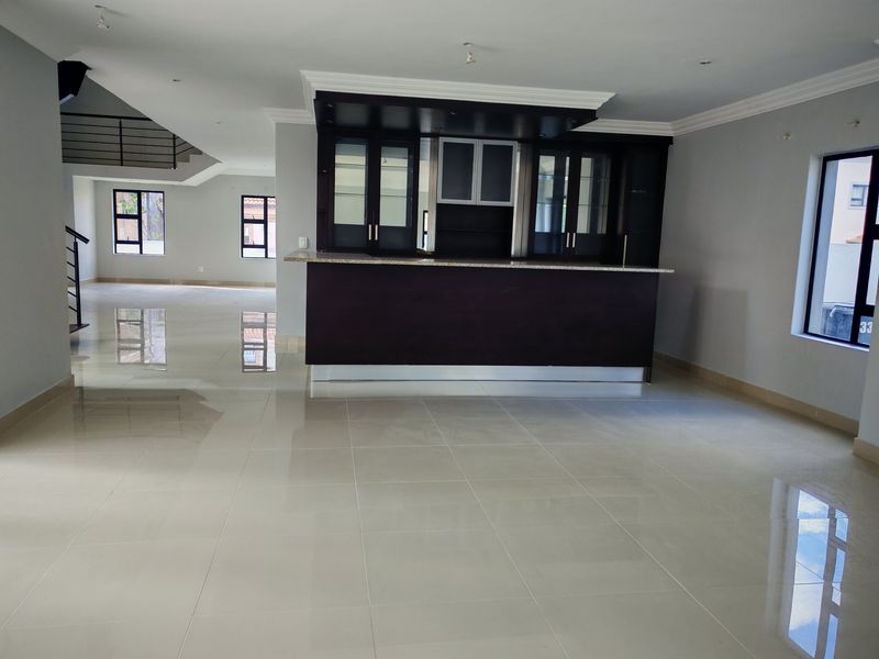 Spacious open-plan living area featuring a built-in bar, polished tile flooring, and modern staircase, offering a clean and versatile layout.