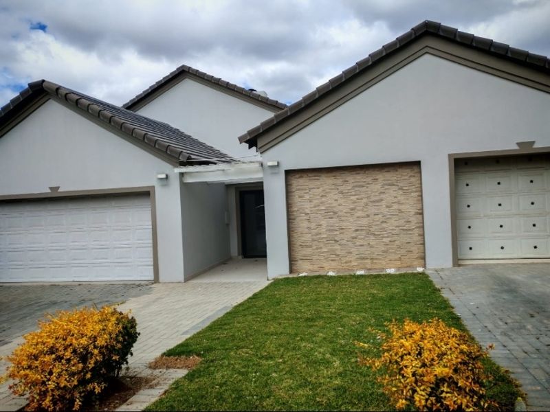 Front elevation of a modern house featuring a paved driveway, double garage doors, and a decorative stone-clad facade.