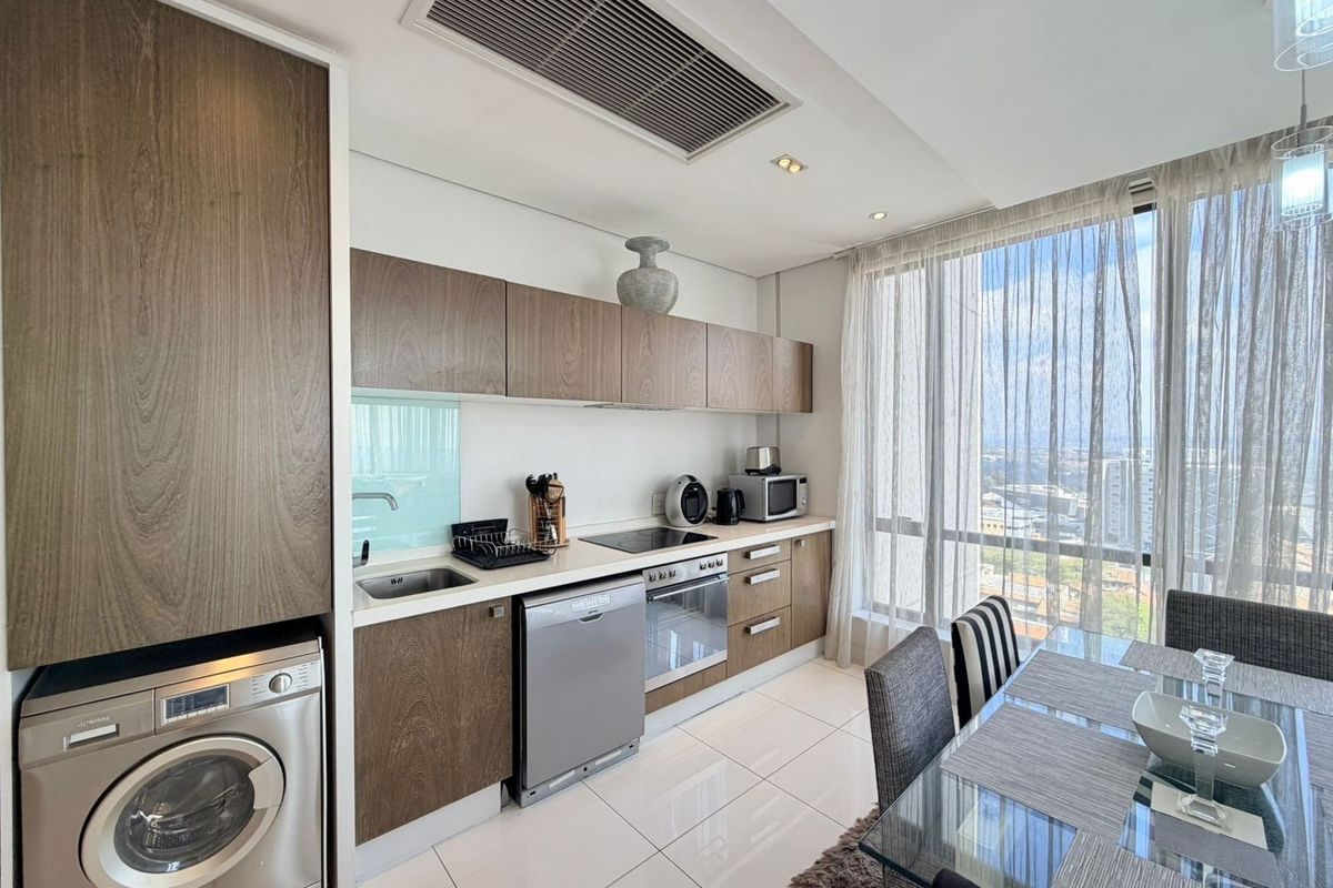 Modern open-plan kitchen featuring sleek wood-finish cabinetry, integrated appliances, and floor-to-ceiling windows with city views, seamlessly connected to the dining area.
