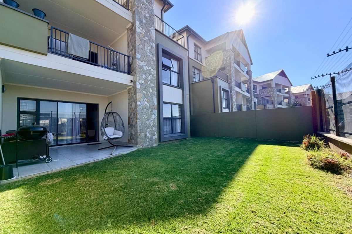 A well-maintained rear exterior view of the apartment featuring a private garden, tiled patio area, and stone-clad architectural detailing.