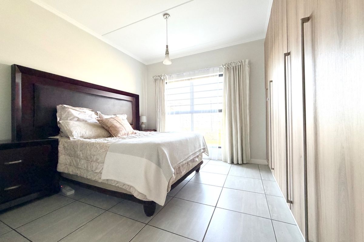 A well-maintained bedroom featuring neutral tiled flooring, ample built-in cupboard storage, and natural light through a large window.