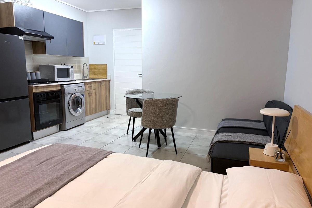 Open-plan studio apartment featuring a compact kitchenette with built-in cabinetry, integrated oven, extractor fan, and laundry facilities, seamlessly connected to the living and sleeping area.