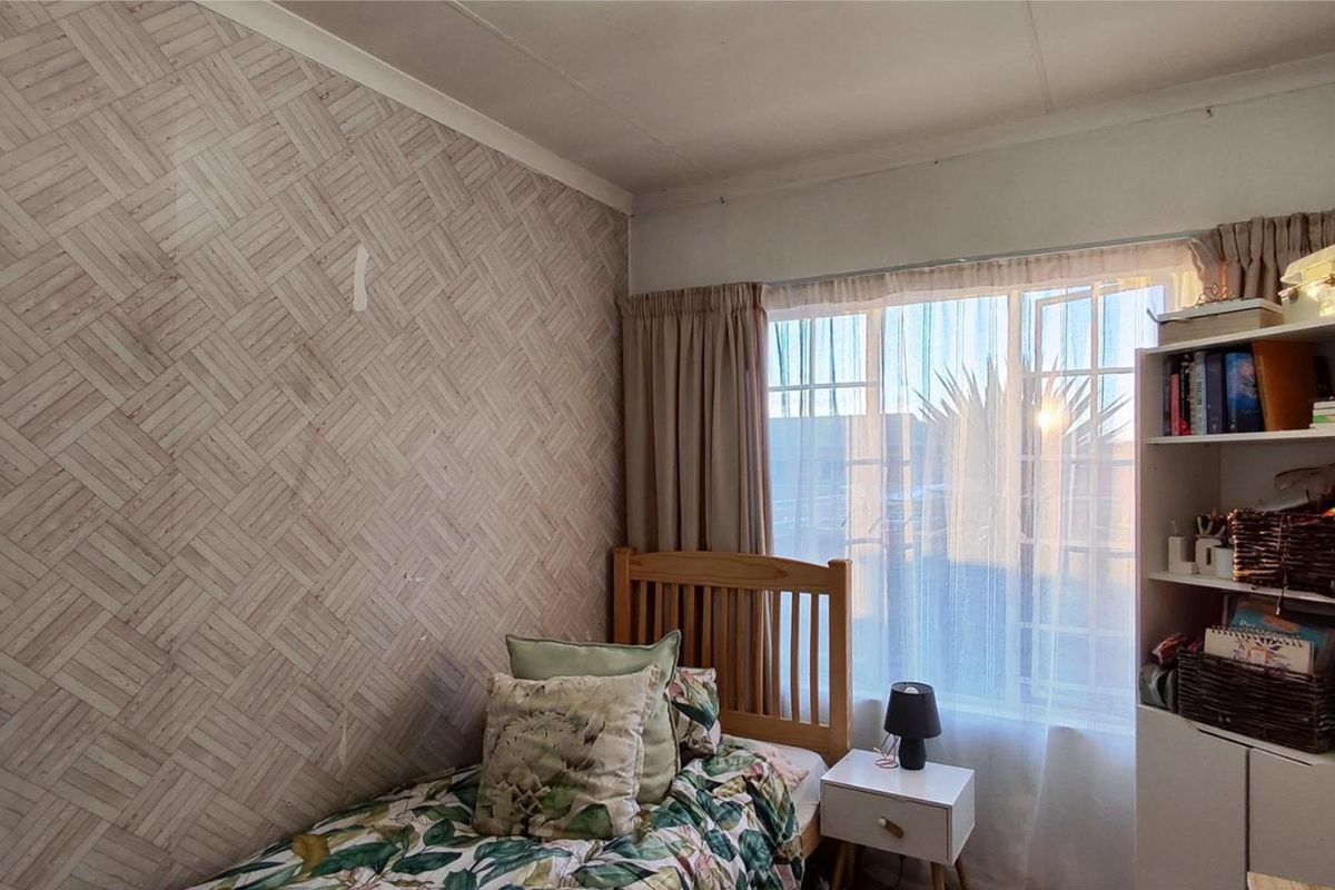 A bedroom featuring textured wallpaper and a large window with curtain rails, providing natural light.