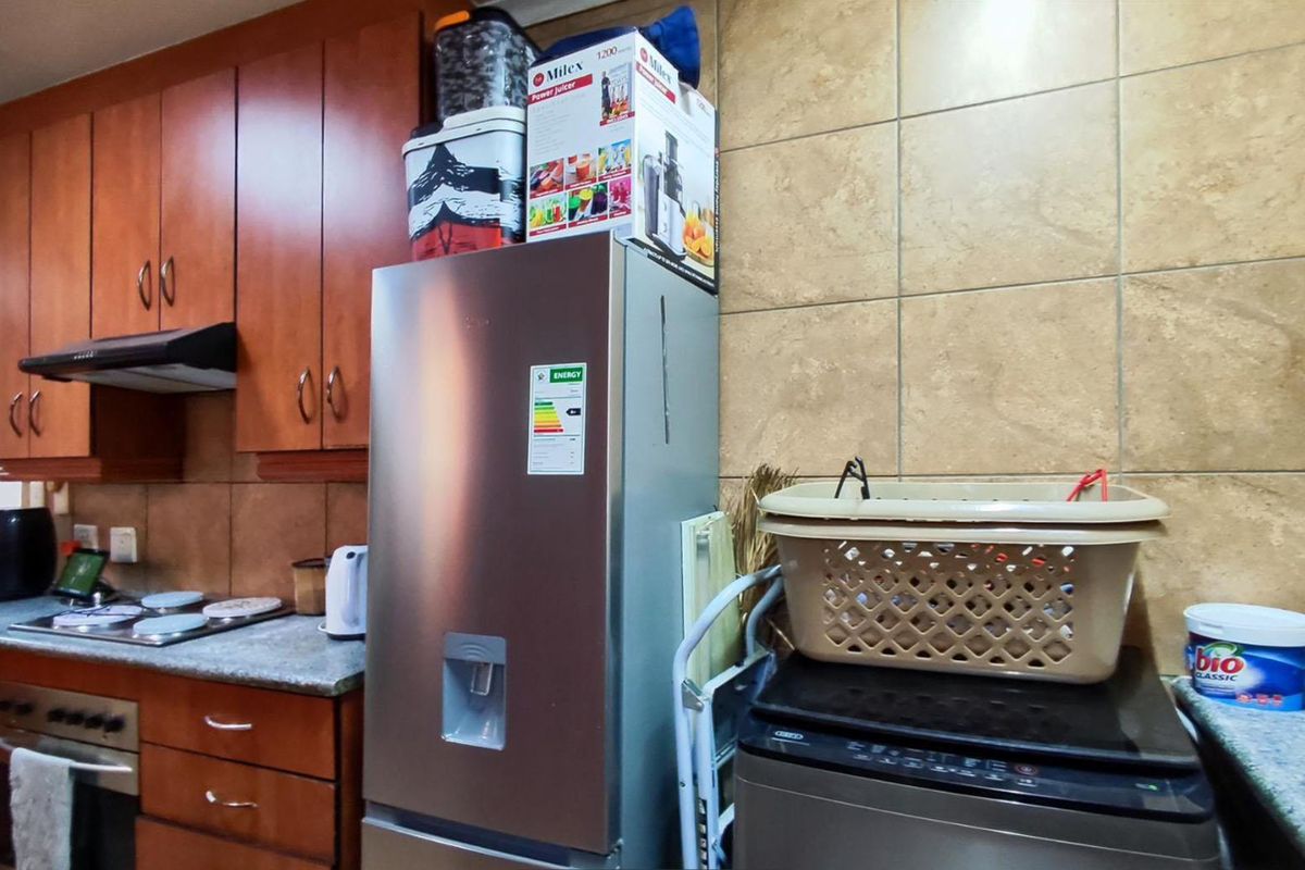 A functional kitchen featuring wood-finish cabinetry, stone countertops, tiled backsplash, and integrated cooking appliances including a hob and oven.