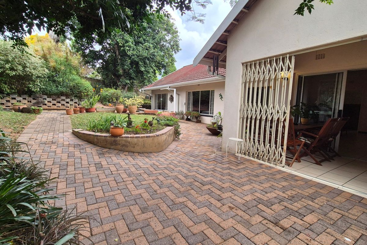 A spacious rear patio featuring brick paving, a low retaining wall, and direct access to the home through sliding glass doors with security gates.