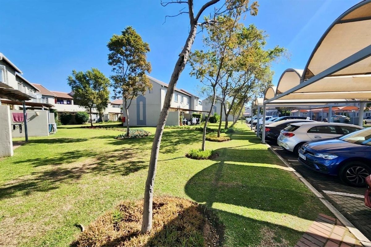 A view of the communal garden area featuring well-maintained lawns, mature trees, and covered parking bays for residents.