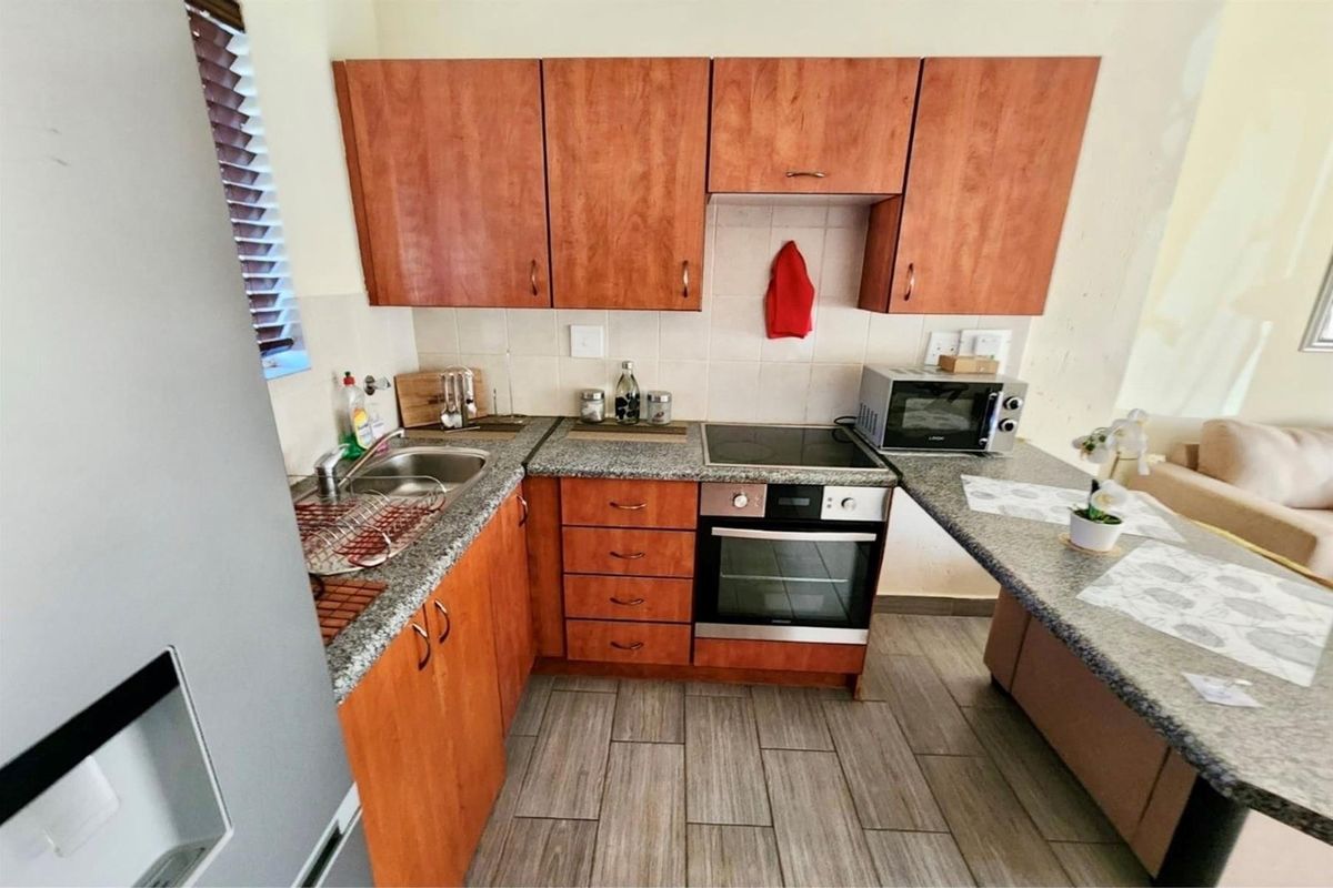Compact kitchen featuring wood-look laminate cabinetry, granite countertops, built-in electric oven and hob, and tiled flooring.