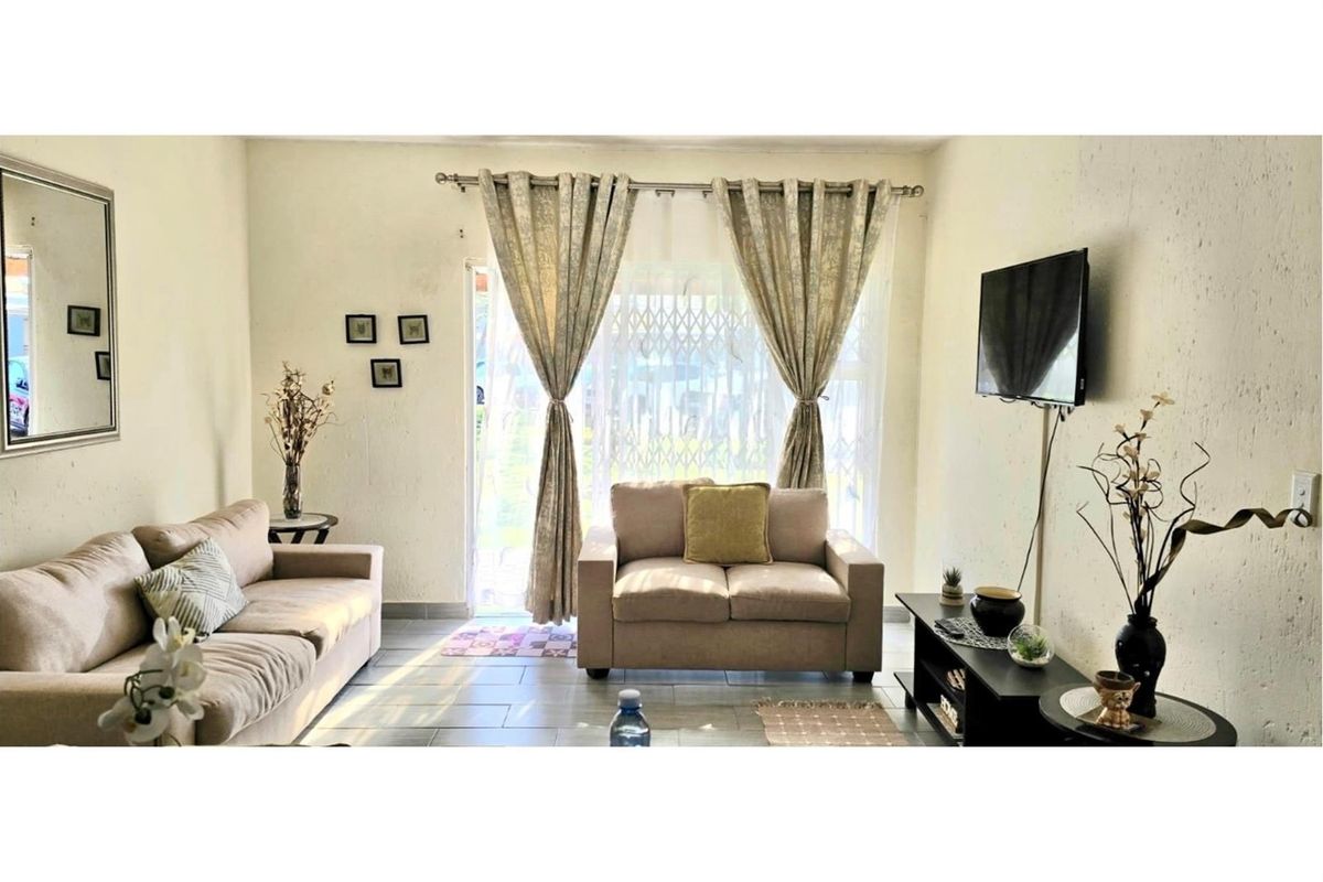 A comfortable living room featuring tiled flooring and a sliding glass door with a security gate, providing access to the exterior.