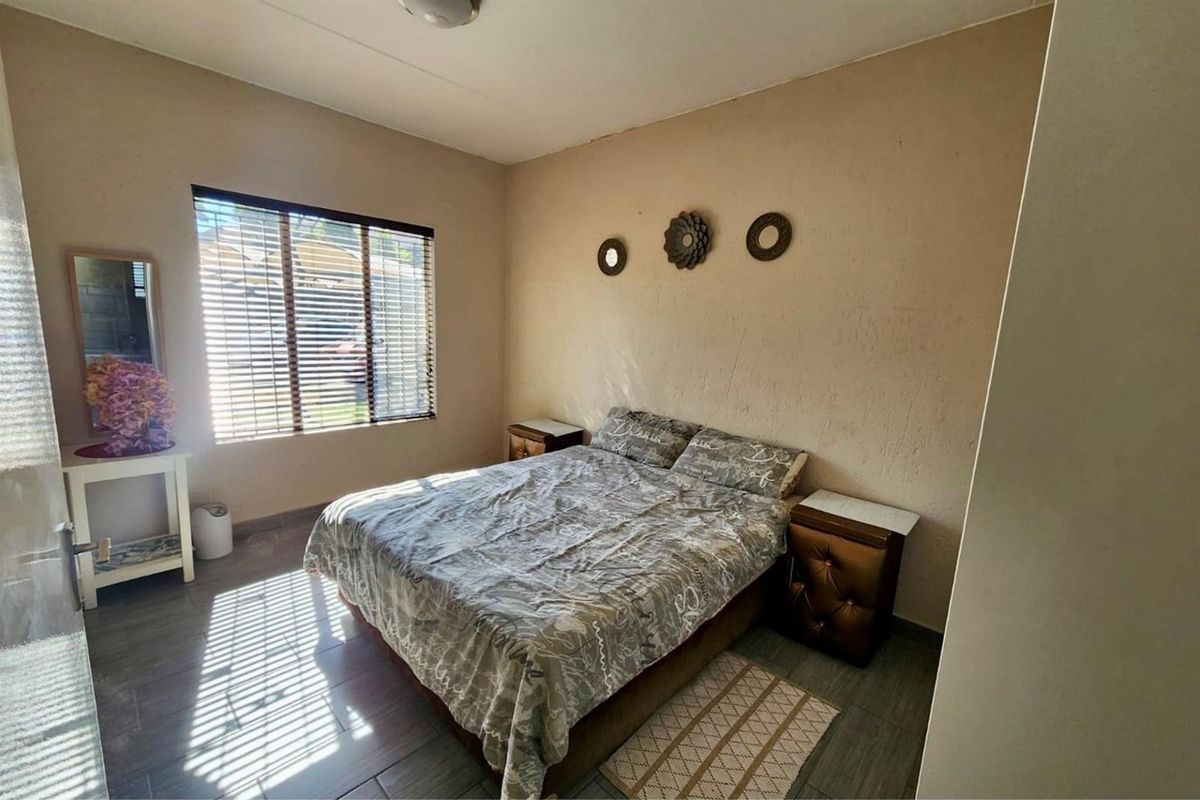 A bedroom featuring tiled flooring and a window with venetian blinds, showing signs of wear on the wall surfaces.