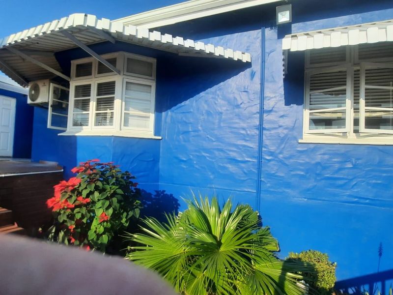 Rear exterior view of the house featuring blue painted walls, metal window awnings, and casement windows with an external air conditioning unit.