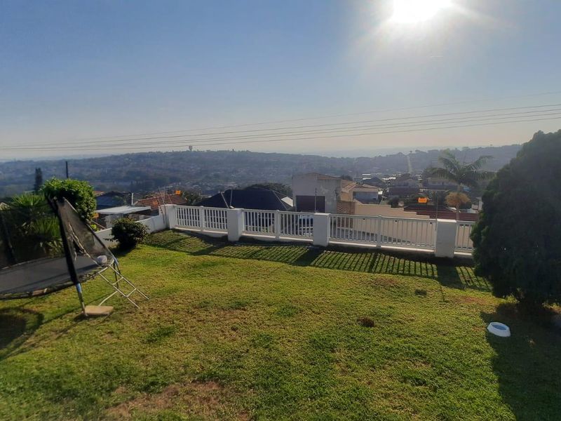 A spacious backyard garden featuring a lawn and a white balustrade railing overlooking the surrounding neighbourhood.