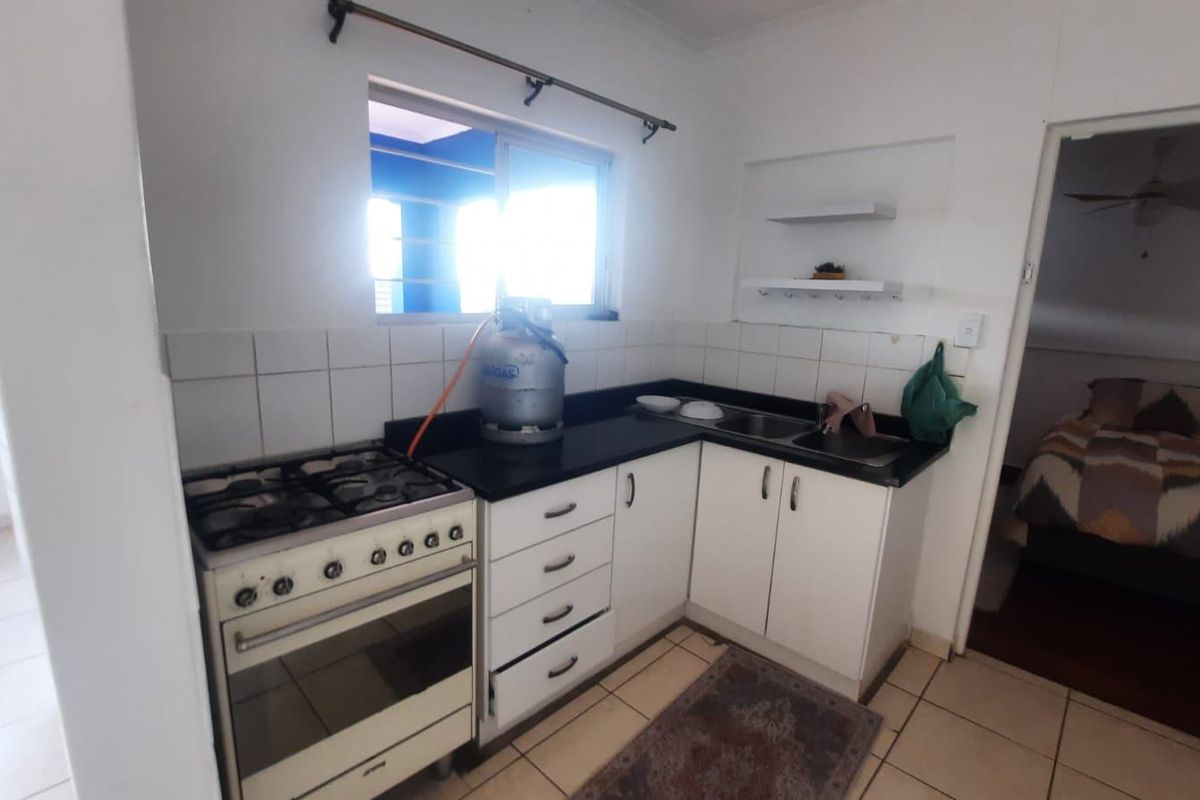 A functional kitchen featuring a gas stove, double sink, tiled backsplash, and built-in cabinetry with floating shelves, providing a practical workspace.
