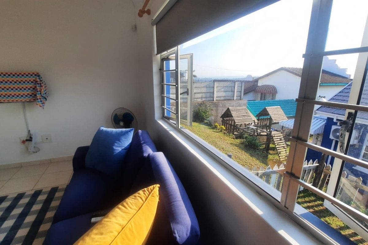 A living room area featuring tiled flooring and a large window with security bars, offering a view of the rear garden and neighboring properties.