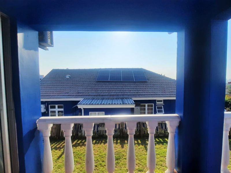 A covered balcony featuring concrete balustrades and pillars, offering a view of the adjacent property with a tiled roof and solar panel installation.