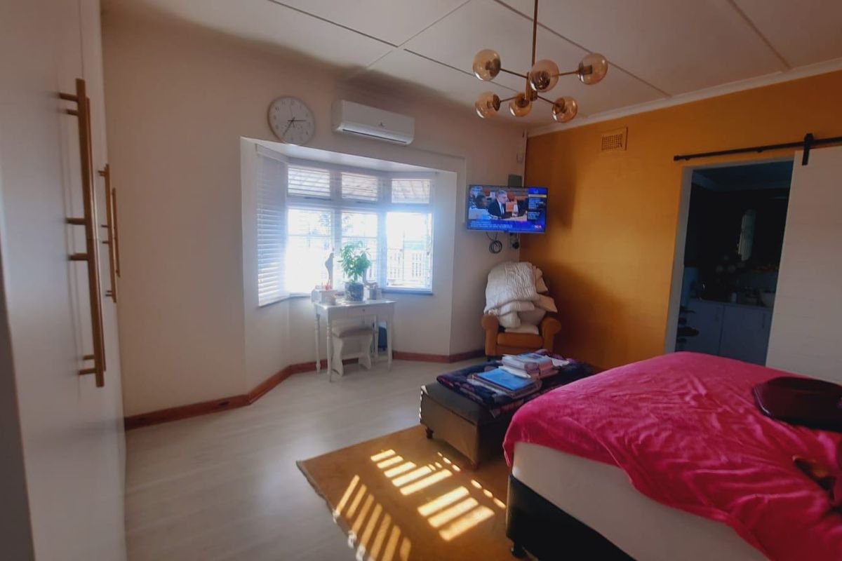 A well-lit bedroom featuring built-in cupboards, a bay window, a split-system air conditioner, and a modern ceiling light fixture.