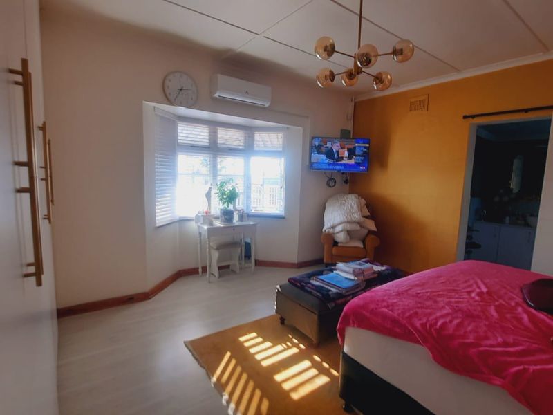 A well-lit bedroom featuring built-in cupboards, a bay window, a split-system air conditioner, and a modern ceiling light fixture.