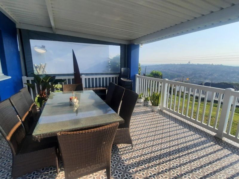 A covered outdoor patio featuring patterned floor tiles, a protective railing, and expansive elevated views of the surrounding area.