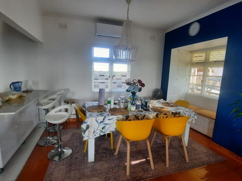 Open-plan dining and kitchen area featuring hardwood floors, a built-in window seat, and a breakfast bar, creating a functional and connected living space.