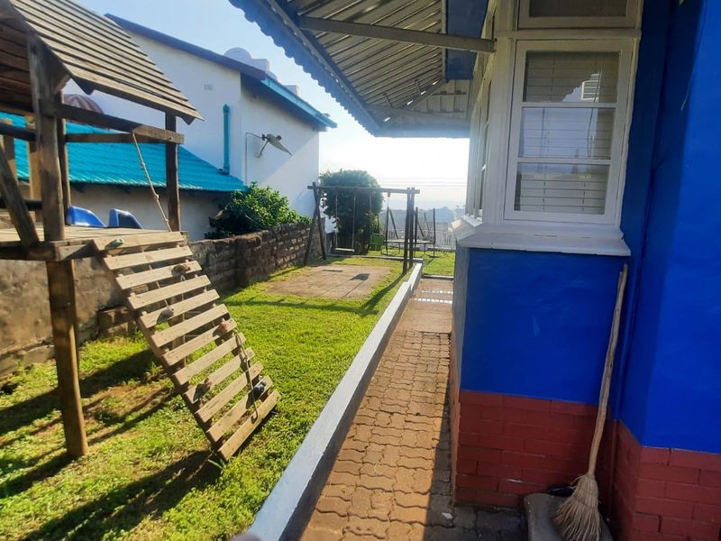 A view of the rear exterior of the house featuring a paved walkway, brick and painted wall finishes, and a small garden area.