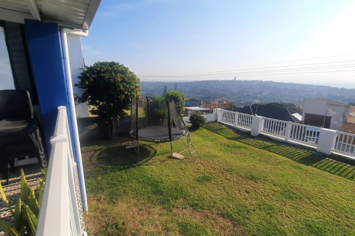 A rear garden area featuring a lawn, white balustrade fencing, and elevated views over the surrounding neighborhood.