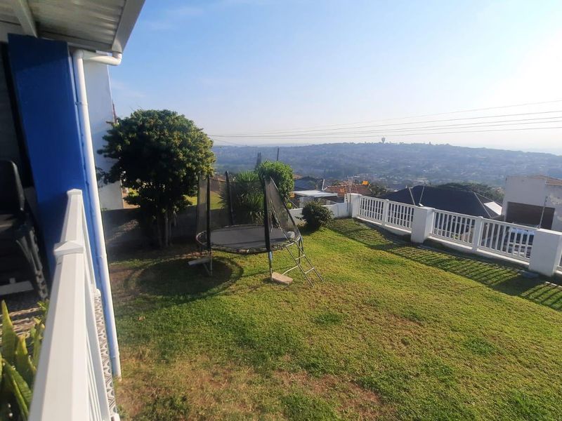 A rear garden area featuring a lawn, white balustrade fencing, and elevated views over the surrounding neighborhood.